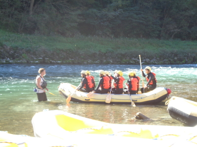 ヘルメットと救命胴衣を身に着けた生徒達が、黄色いボートに乗って川の中に入り、オールで漕ぎだそうとしている写真