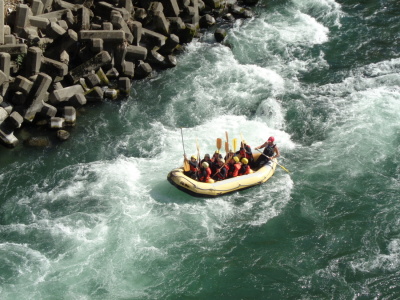濁流の中で生徒達がオールを上に持ち上げ、ボートが川を下っている様子の写真