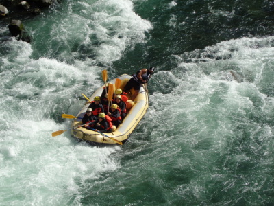 濁流の中、ボートに乗っている生徒達がオールを上にあげて川を下っている様子の写真