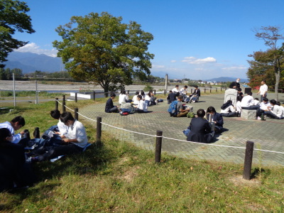 アスファルトの広々としたスペースで、友達同士で分かれて座り、お弁当を食べている様子の写真