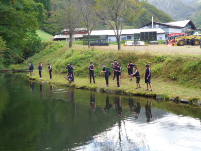 ジャージ姿の生徒たちが川に沿って並び川釣りをしている写真