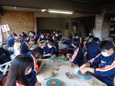 ジャージ姿の生徒たちが、土を丸めたり形を形成して陶器を作っている様子の写真