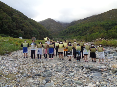 山並みを背景にして手に黄色の布を持った生徒たちが横2列になって記念撮影をしている写真