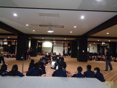 広い会場に多くの生徒が座っており、会場の中央でマイクを持った生徒が話をしている写真