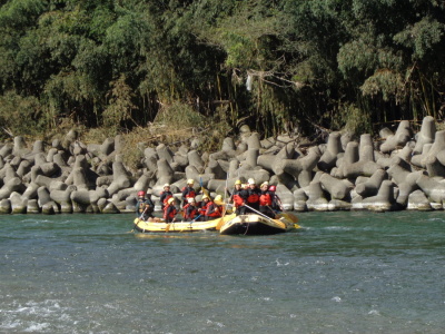 2隻のボートが川を下っており、ボートの中で生徒達が立ってボートを漕いでいる写真