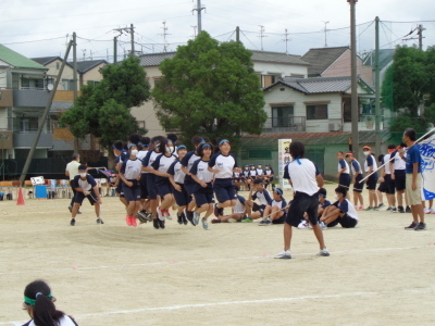 校庭で青組の生徒たちが大縄跳びで一斉に飛んでいる瞬間の写真
