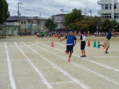 青のビブスを着た男子生徒がゴールテープを切ってゴールした瞬間の写真