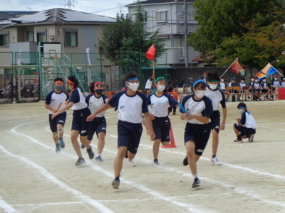 リレーバトンの受渡し地点で男子生徒からバトンを受け取って走り出す女子生徒たちの写真