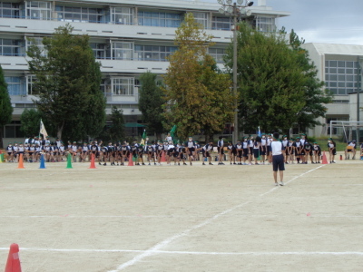 校庭で緑の鉢巻をした生徒たちが横一列になって準備運動をしている写真