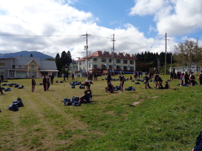 芝生の上にリュックが置かれ、生徒たちが散らばって立っている写真