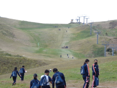 右側に等間隔に並んだリフトが写っている丘の道を生徒たちが登っている写真
