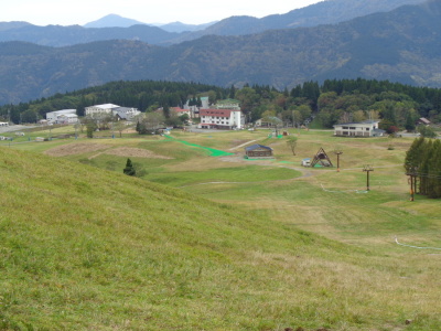 奥に山や、白い建物が見え、手前には芝生が一面に広がっている丘を写した写真