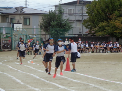 青の鉢巻をした生徒がバトンを受け先頭を走っている写真