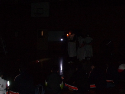 真っ暗闇の中をキャンドルを持った3名の生徒たちが歩いている写真