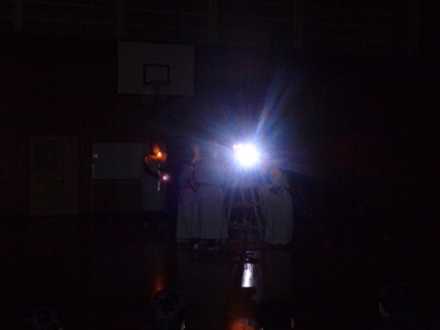 暗闇の中で立っている白い服を着た生徒たちの間に光が差し込んで光っている写真