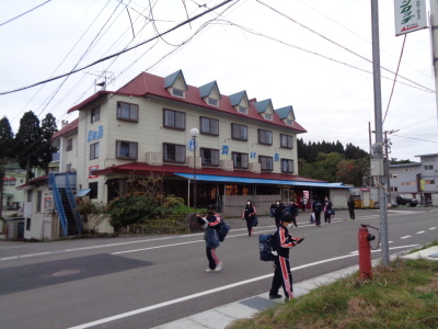 生徒たちが手に持った紙のようなものをみながら道路を渡っている写真