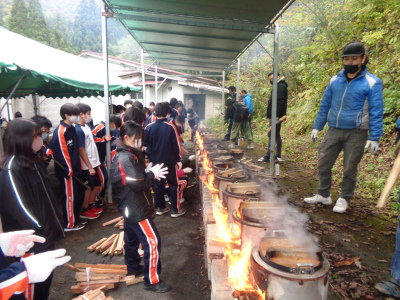 軍手をした生徒たちが釜戸の火の様子を見ている写真