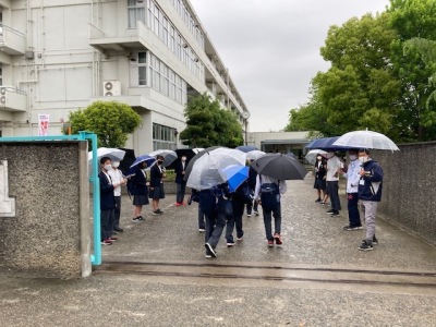 校門の中で教員や生徒が見守るなか傘を差して登校している生徒たちの写真