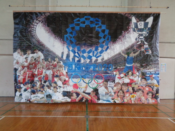 中央に東京オリンピックのロゴマーク、周囲に選手たちを描いた展示作品の写真