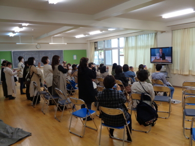 大きなテレビに映し出された映像をそれぞれ保護者がビデオやスマートフォンなどで撮影している写真