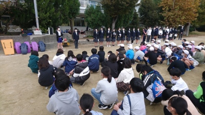 校庭に座っている小学生の前で生徒たちが横一列に並んでいる写真