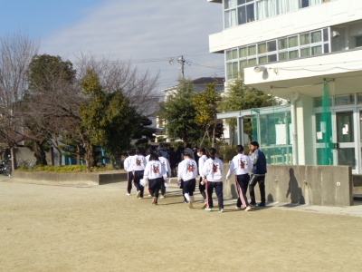 白いトレーナー姿の参加者たちが校舎の前を歩いている写真