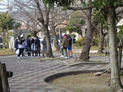 まばらに立っている数本の木の奥に白い帽子を被った生徒や学生服姿の参加者たちがゴミ拾いをしている写真