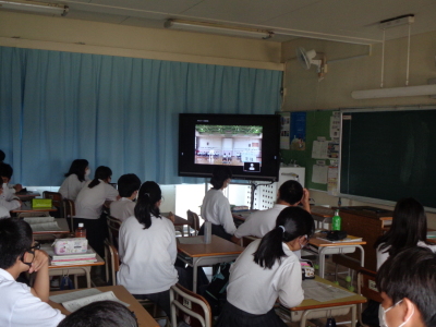 体育館で行われている生徒総会の様子を教室のテレビ画面で見ている生徒たちの写真