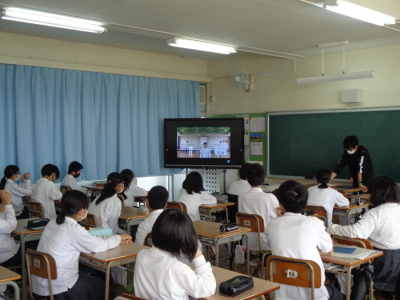 教室で自席についている生徒たちがモニターに映し出されている生徒総会を見ている写真
