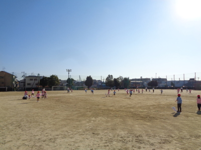 大きなグラウンドを凧を持って駆け回っている園児の写真