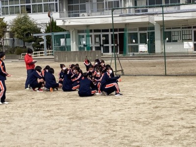 グラウンドに置かれた防球ネットの前の地面に女子生徒たちが座っている写真