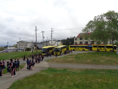 4台の黄色のバスから生徒たちが降りてきて広場に向かって歩いている写真