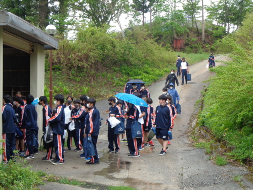 雨が降るなか荷物を持ち左側の建物の中に入っていく生徒たちの写真