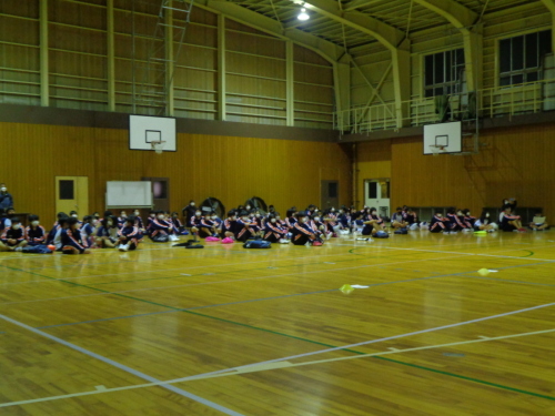 体育館の床に体育座りしている生徒たちの写真