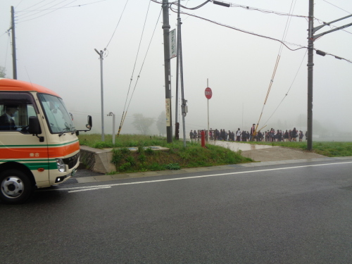 周囲が霧がかかった芝生広場に集合している生徒たちを道路の反対側から撮影した写真