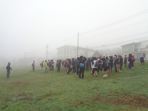 霧がかかっている芝生広場に集まってきた生徒たちの写真