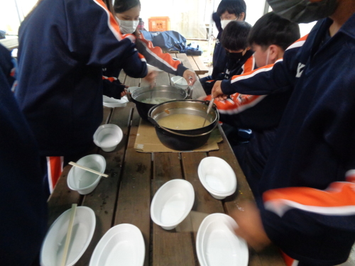 2つの鍋をダンボールの上に置き完成した料理をお玉でついでいる生徒たちの写真