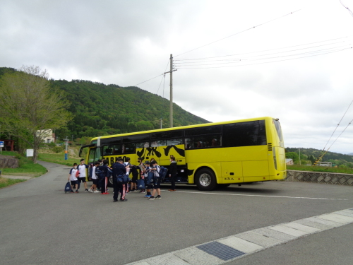 バスが到着しバスから降りた生徒たちが荷物を持っている写真