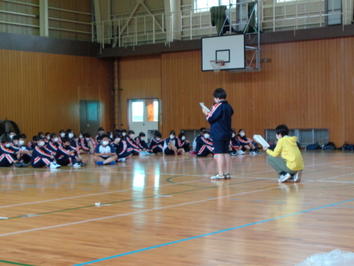 床に座っている生徒たちが前に立っている女子生徒の話を聞いている写真