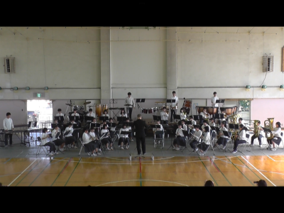 指揮者が中央に立ち、生徒たちが楽器を演奏している写真