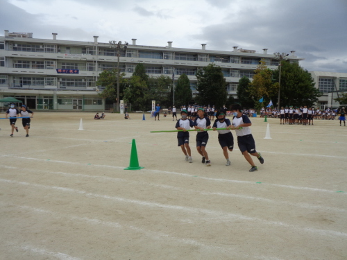 緑組の女子生徒4人が緑の長い棒を持ち、コーンの周りを走っている写真