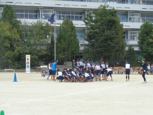 2人の生徒が持った青の長い棒を並んでいる青組の生徒たちが順番に飛び越えている写真