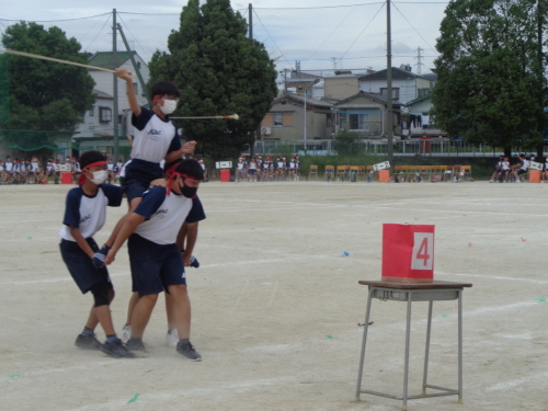 三人の生徒の上に乗った赤組の生徒がロープを上にあげ、赤い箱に当てようとしている写真