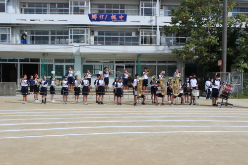 校舎前の屋外で演奏を行っている吹奏楽部の部員の写真