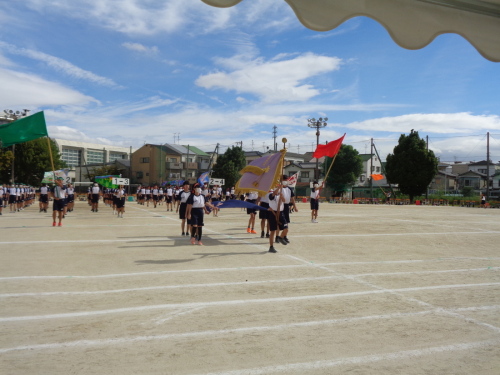 優勝旗を持った生徒や赤や緑の団旗を持った生徒に続いて、整列した生徒たちが行進をしている写真