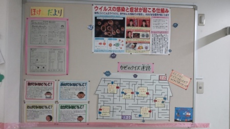 ウイルスの顕微鏡の写真が載っているポスターとかぜのクイズ迷路、ほけんだよりが掲示されている掲示板の写真