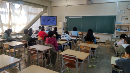 教室のモニターに映像が映され、児童の皆さんが席に着き、学習している様子を後方より写した写真