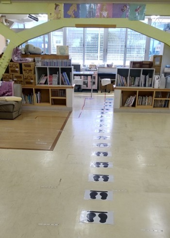 本棚に本が並んでおり、床に、間隔をあけて立つための足跡の印が貼られている保険室の写真