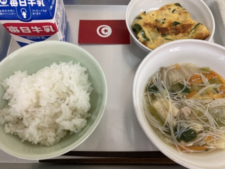 チュニジアの小さな国旗が置かれたトレイに並べられた、ごはん・牛乳・ビーフンスープ・タジンの給食の写真