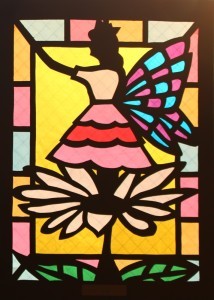 チョウの羽のようなものがある女性が、花の上に立っているステンドグラスの作品の写真